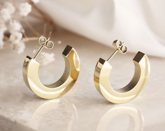 May include: A pair of gold hoop earrings with a thick, rounded design. The earrings are made of metal and have a polished finish.