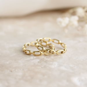 May include: Two gold chain rings stacked on top of each other. The rings are made of a series of connected oval shapes.