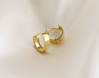 Puede incluir: Un par de pendientes de aro de oro. Los pendientes son simples y elegantes, con un acabado liso y pulido.