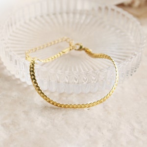 May include: A gold chain bracelet with a delicate, slightly curved, link design.