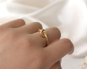 May include: A gold knot ring on a finger.