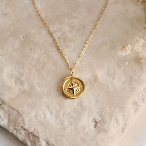 May include: A gold necklace with a compass pendant. The compass is a round, flat disc with a raised star in the center and four points.