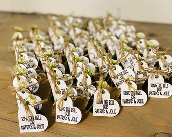 Op de afbeelding: Een verzameling witte hartvormige kaartjes met de tekst "Ring the bell for Patrick & Jolie" vastgebonden met touw en kleine takjes groen.