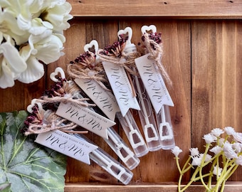 May include: Four clear plastic bubble wands with heart-shaped handles, each tied with twine, a small bunch of dark red dried flowers, and a white tag printed with the text "Mr & Mrs" and "Bubbles and wishes for the Mr & Mrs".