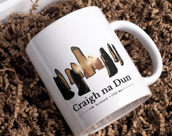 May include: White ceramic mug with a black and brown illustration of the Craigh na Dun standing stones from the Outlander TV series. The text "Craigh na Dun" is printed in black with the words "Scotland 1743" underneath.