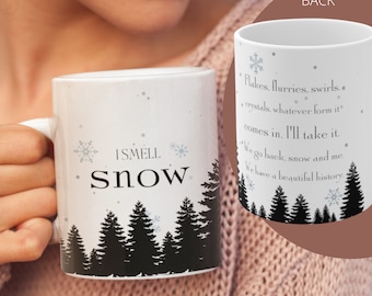 May include: White ceramic mug with a black silhouette of a forest and the text "I smell snow". The back of the mug has a quote about snow: "Flakes, flurries, swirls... crystals, whatever form it comes in. I'll take it. We go back, snow and me. We have a beautiful history."