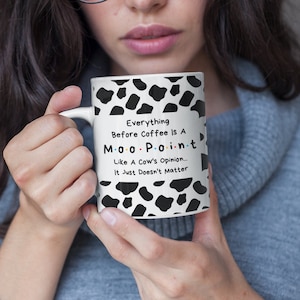 Peut inclure: Une tasse en céramique blanche avec un motif de vache noir et blanc. La tasse porte l'inscription "Everything Before Coffee Is A Moo-Pain-t Like A Cow's Opinion... It Just Doesn't Matter".