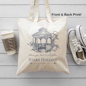 May include: A white canvas tote bag with a blue illustration of a gazebo and the text "Where you lead, I will follow. STARS HOLLOW - FOUNDED 1779".