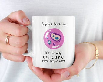 May include: White ceramic mug with a pink and purple bacteria illustration and the text "Support Bacteria It's the only culture some people have".