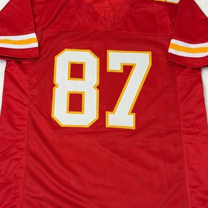May include: A red football jersey with the number 87 in white with a yellow outline on the front. The number 7 is on the left shoulder and the number 8 is on the right shoulder. The sleeves have white and yellow stripes.