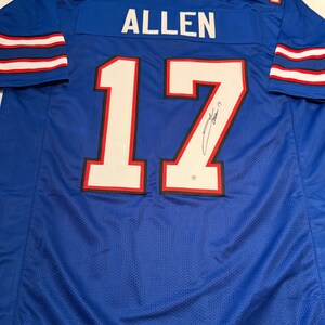 Puede incluir: Una camiseta de f&uacute;tbol azul con el nombre "ALLEN" y el n&uacute;mero "17" en blanco. La camiseta tiene rayas rojas y blancas en las mangas y el n&uacute;mero "17" est&aacute; delineado en rojo. La camiseta parece estar firmada.