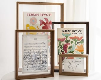 Könnte beinhalten: Vier Holzrahmen mit Glasfronten, die verschiedene Kunstwerke zeigen. Der obere Rahmen zeigt ein Poster mit dem Text "FLOWER MARKET" in umgekehrter Reihenfolge. Der mittlere Rahmen zeigt ein Notenblatt. Der untere Rahmen zeigt eine Zeichnung eines Vogels. Der Rahmen rechts zeigt ein farbenfrohes Poster mit dem Text "BOLOGNA FLOWER MARKET" in umgekehrter Reihenfolge.