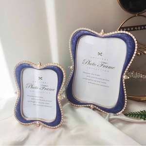 Op de afbeelding: Twee sierlijke fotolijsten met een blauwe en gouden afwerking. De lijsten zijn versierd met nepparels en hebben een gegolfde rand. De grotere lijst heeft de tekst "ORIGINAL Photo Frame COLLECTION" en de kleinere lijst heeft de tekst "ORIGINAL Photo Frame COLLECTION".