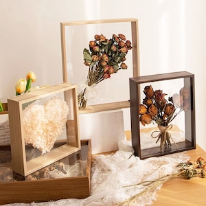 Puede incluir: Varios marcos de caja de sombra con flores secas y un arreglo floral en forma de corazón. Los marcos son de madera y tienen frentes de vidrio transparente. Las flores son de varios tonos de marrón y beige.