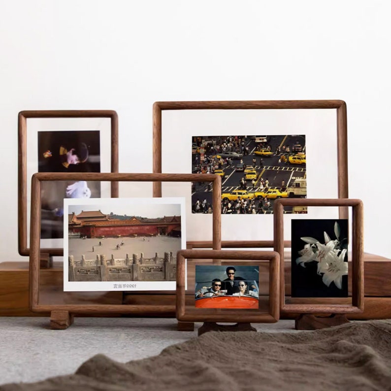 May include: Five wooden picture frames with glass fronts, each displaying a different photograph. The frames are all different sizes and are arranged in a staggered formation. The photos include a cityscape, a building with a red roof, a group of people in a car, and a bouquet of white flowers.