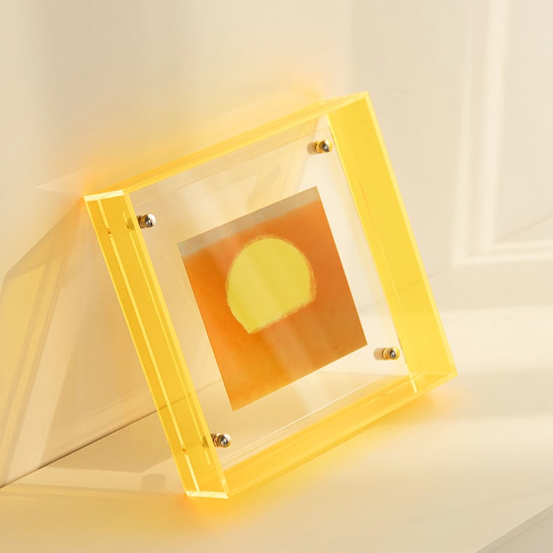 Puede incluir: Un marco de fotos de acr&iacute;lico amarillo con un frente transparente y una imagen de puesta de sol amarilla en el interior.