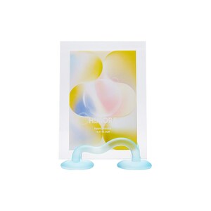 May include: A clear glass photo frame with a blue and yellow abstract design. The frame is 10.2 x 15.2 cm and has a blue plastic stand.