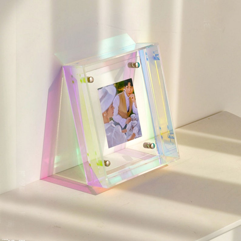 Op de afbeelding: Iridescent acryl fotolijst met een foto van twee personen. De lijst heeft een transparante voor- en achterkant met een kleurrijke, regenboogachtige glans. De lijst wordt bij elkaar gehouden door zilverkleurige hardware.