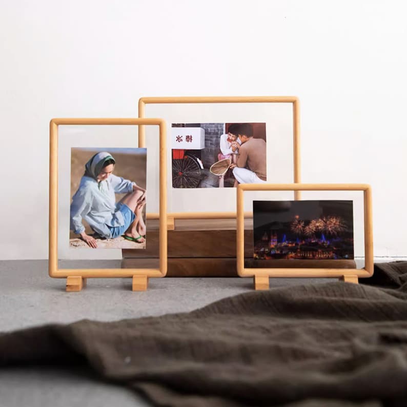 May include: Three wooden picture frames with different photos inside. The frames are standing on a brown surface. The photos show a woman sitting on the ground, a couple walking down a street, and fireworks over a city.