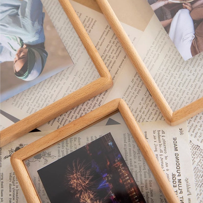 May include: Four wooden picture frames in various sizes and orientations, arranged on a printed page. The frames are made of natural wood with a light brown finish. The frames are empty, but there are glimpses of photos inside.