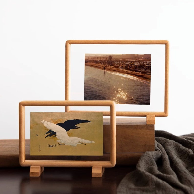 May include: Two wooden picture frames with glass fronts, one with a black and white bird illustration and the other with a photograph of a beach scene.