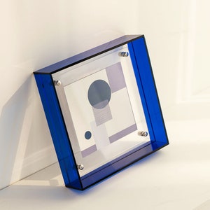 Puede incluir: Un marco de fotos de acr&iacute;lico azul con un dise&ntilde;o geom&eacute;trico impreso en el interior. El marco tiene tornillos plateados en las esquinas.