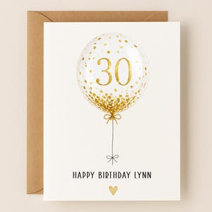 May include: A birthday card with a gold foil balloon design. The balloon has the number 30 in gold, with gold confetti. The card reads "Happy Birthday Lynn" with a gold heart below.
