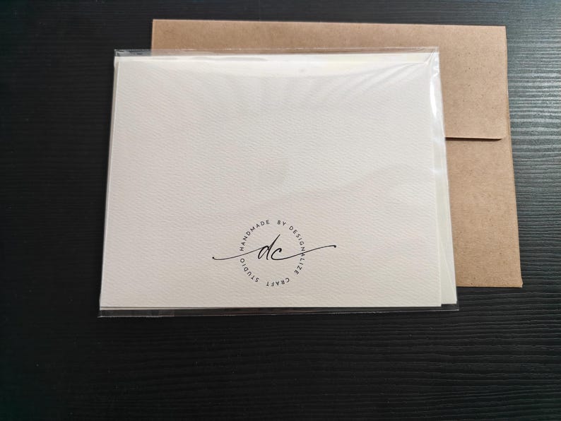 May include: A stack of off-white cards in a clear plastic sleeve, with a brown paper envelope. The cards have a textured surface and a circular logo that reads "HANDMADE BY DESIGNALIZE CRAFT" with the initials "dc".