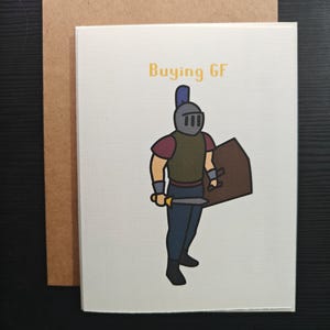 May include: A greeting card with a cartoon illustration of a knight in armor holding a sword and shield. The text "Buying GF" is written in yellow at the top of the card.
