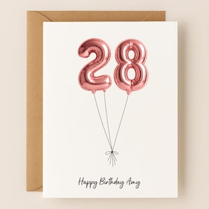 May include: A birthday card with a white background and a brown envelope. The card features two rose gold number 28 balloon illustrations tied together with black string. The words "Happy Birthday Amy" are written in black script.