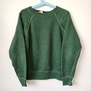 May include: A forest green long-sleeve sweatshirt featuring a crew neckline and raglan sleeves. The garment is constructed with visible light green contrast stitching along the seams of the sleeves and sides, finished with ribbed cuffs and hem.