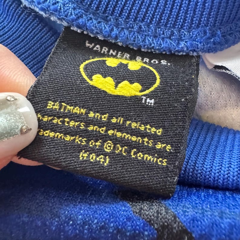 May include: A black tag with the Batman logo in yellow, and the text "WARNER BROS." is visible. The tag also includes the text "BATMAN and all related characters and elements are trademarks of &copy; DC Comics (s04)".