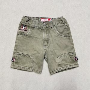 Pode incluir: Shorts cargo verdes com patches vermelhos e brancos. Os patches têm o texto "Otaku!" e um gráfico de um personagem de desenho animado.