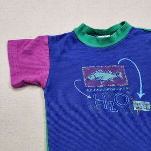 May include: A blue short-sleeved shirt with a green collar and a purple sleeve. The shirt features a fish graphic with the text "FISH FISH FISH FISH FISH FISH" and "H2O".