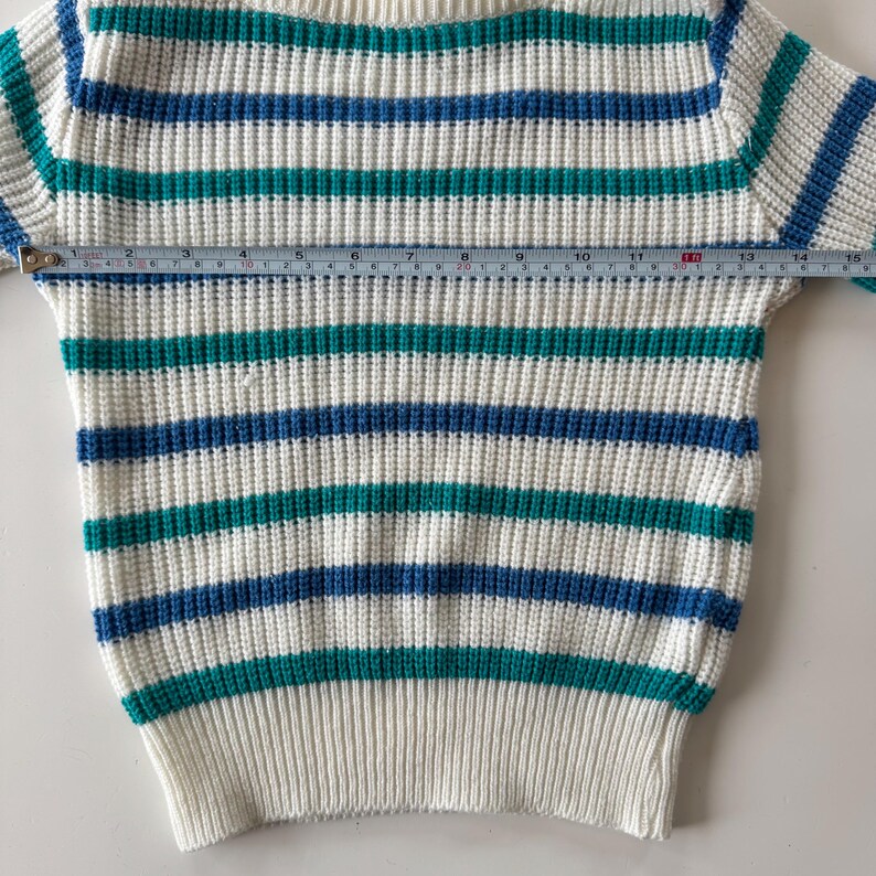 May include: A cream-colored sweater with horizontal stripes in teal and navy blue. The sweater has a ribbed knit texture and a crew neck. The sleeve length is approximately 15 inches.
