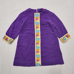 Può includere: Un abito viola a maniche lunghe con un pannello centrale verticale e polsini abbinati di colore giallo, decorato con un motivo ripetitivo di fiori azzurri, viola e bianchi. Il capo presenta uno scollo rotondo e una cerniera sul retro.