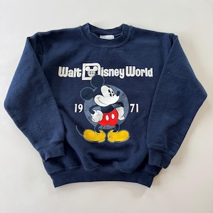 Peut inclure: Une tasse en céramique blanche avec une anse noire et le texte "But First, Coffee" en gras noir. La tasse est posée sur un fond neutre, soulignant son design simple.