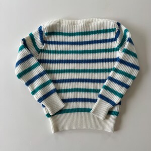 May include: A white sweater with horizontal stripes in teal and blue. The sweater has long sleeves and a ribbed knit design. The cuffs and bottom hem are solid white.