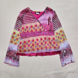 Könnte beinhalten: Ein langärmeliges Oberteil mit V-Ausschnitt und Wickeloptik. Das Kleidungsstück zeigt ein lebhaftes, mehrfarbiges Muster in Pink-, Lila-, Gelb- und Orangetönen, akzentuiert durch ein horizontales Paillettenband im mittleren Bereich.