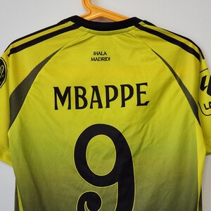May include: A yellow and black soccer jersey featuring the name MBAPPE and the number 9 printed in black on the back. The text &iexcl;HALA MADRID! is printed in black near the neckline, with black mesh side panels and black shoulder stripes.