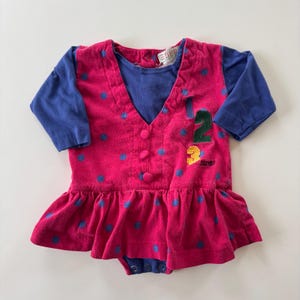 May include: A vintage baby outfit featuring a pink bodice with blue polka dots and a ruffled skirt. The outfit has a blue long-sleeved undershirt and is adorned with the numbers "1, 2, 3" in green and yellow. The brand "ESPRIT" is visible.