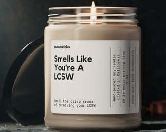 May include: A beige soy candle with a glass jar and a black lid. The candle is labeled "Smells Like You're A LCSW" and has a 50-60 hour burn time. The candle is hand-poured in California.
