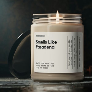 May include: A beige soy candle in a glass jar with a black lid. The candle is labeled "Smells Like Pasadena" and has the text "Hand-poured soy candle, crafted in California, 50-60 hours burning time, 9 oz, Keep away from flammables".
