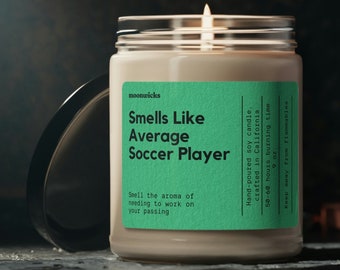 May include: A green and white candle with the text "Smells Like Average Soccer Player" and "Hand-poured soy candle, crafted in California 50-60 hours burning time".