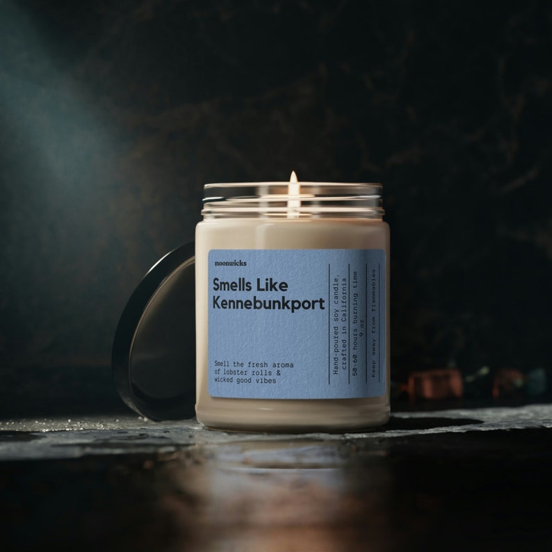 May include: A beige soy candle in a glass jar with a blue label that reads "Smells Like Kennebunkport". The label also says "Hand-poured soy candle, crafted in California, 50-60 hours burning time, 9 oz".