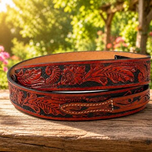 May include: A coiled leather belt featuring a deep red and black finish with intricate floral and leaf tooling patterns embossed across the surface. The belt displays a pointed tip and visible stitching along the edges of the leather strap.