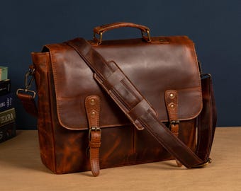 May include: A brown leather messenger bag with a long adjustable strap, two buckles, and a top handle. The bag has a distressed look and is made of high-quality leather.