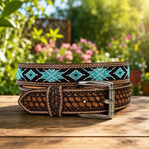 May include: A brown leather belt featuring a basket-weave embossed pattern and a central band of black and turquoise geometric beadwork. The belt includes a silver-toned metal buckle and white contrast stitching along the edges.