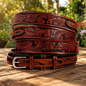 May include: A coiled leather belt featuring a deep brown and black floral embossed pattern. The belt has a polished silver-tone metal buckle and a series of loops, showcasing intricate carved details across the entire length of the strap.