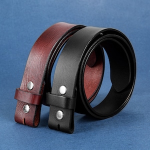 May include: Two leather belts, one black and one brown, are shown lying on a blue surface. The belts are both made of a smooth leather and have a simple design. The belts are both about 1 inch wide and have a buckle on one end.